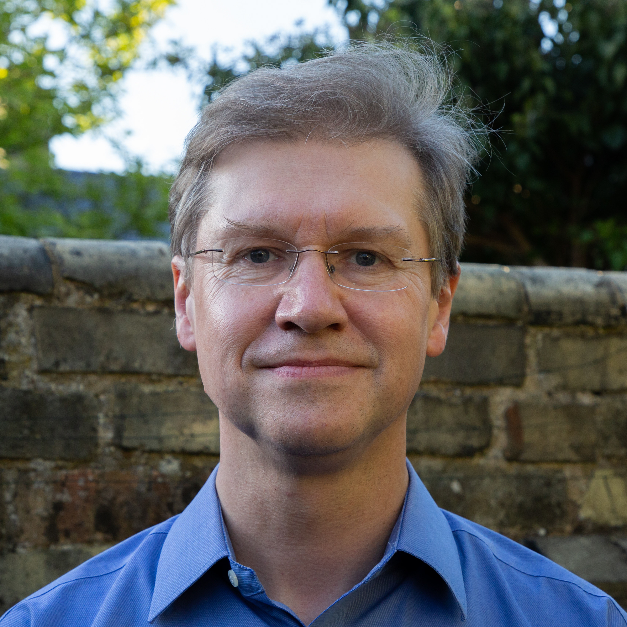 blond man in front of brick garden wall