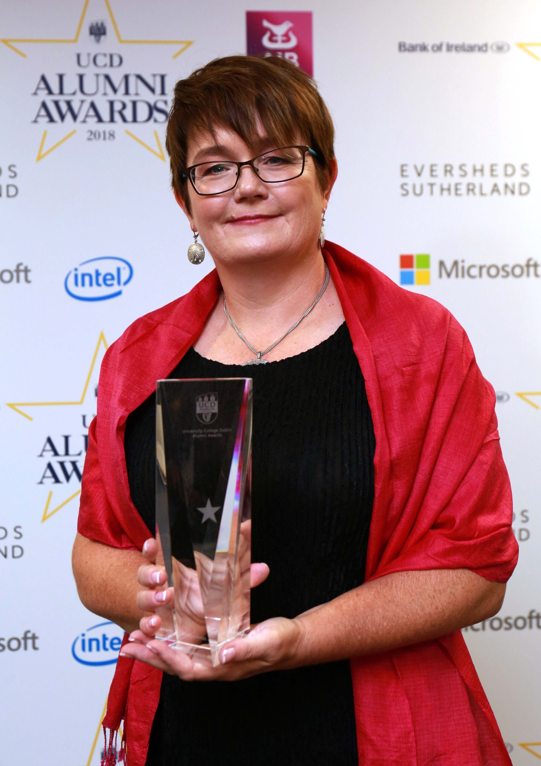 Julie McEnery; short haired woman with red shawl over black dress with crystal-like award