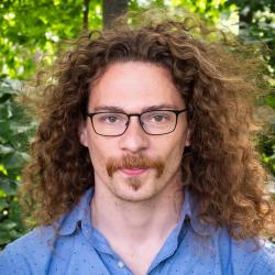 Man with long light brown hair, moustache wearing glasses outside