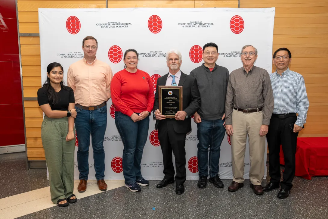 Group of Atmospheric and Oceanic Science colleagues in front of CMNS branded backdrop