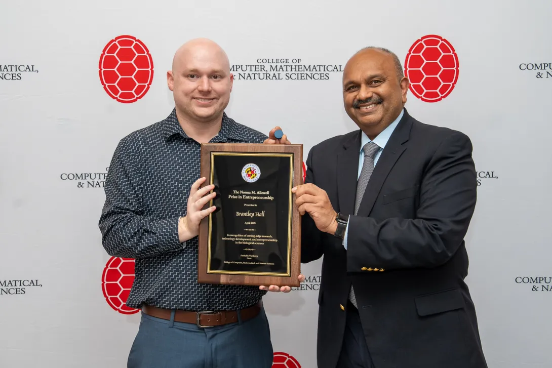 Brantley Hall and Amitabh Varshney holding a plaque in front of a CMNS branded backdrop