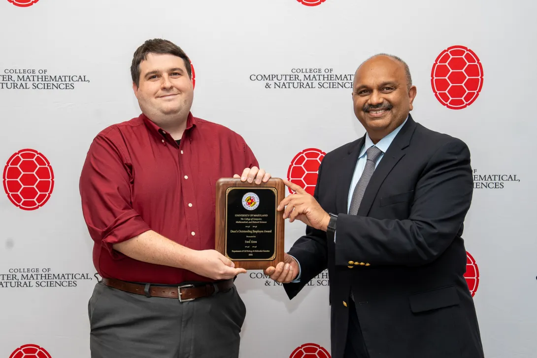 Paul Keen and Amitabh Varshney holding plaque in front of a CMNS branded backdrop